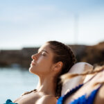 Beautiful girls smiling, sunbathing, lying on chaises near sea.