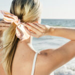 Blonde woman tying a ponytail at the beach back view