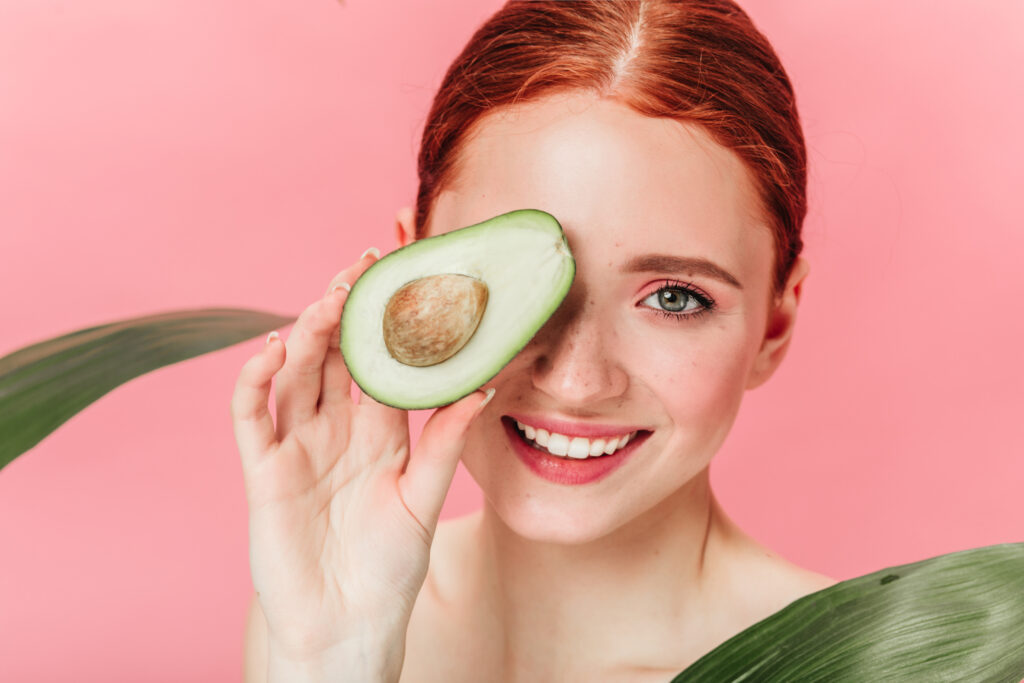 Close up view of gorgeous ginger woman with avocado. Studio shot of excited caucasian girl with healthy food isolated on pink background