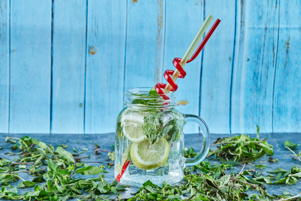 Mojito cocktail with slices of lime and mint on blue table with fresh mint leaves