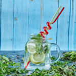 Mojito cocktail with slices of lime and mint on blue table with fresh mint leaves
