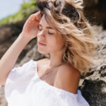 Pleasant girl posing near rock with eyes closed. Outdoor portrait of tanned sensual lady standing on nature background..