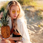lifestyle-outdoor-picture-laughing-pretty-woman-with-juicy-pineapple-relaxing-sunny-beach-trendy-summer-outfit