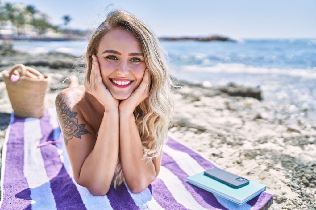Young blonde girl wearing bikini lying on the towel at the beach.