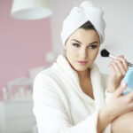 Young beauty adding blusher to her cheeks