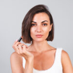 Close beauty portrait of woman with makeup and brown lipstick on gray background